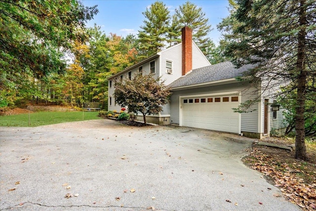 view of side of property with aphalt driveway, a chimney, and an attached garage