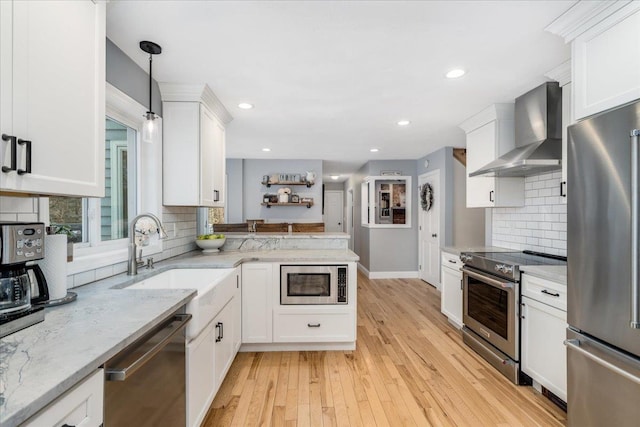 kitchen with light wood-style floors, appliances with stainless steel finishes, wall chimney range hood, white cabinetry, and a sink