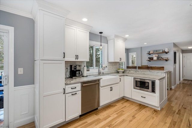 kitchen featuring a peninsula, a sink, white cabinets, appliances with stainless steel finishes, and light wood finished floors