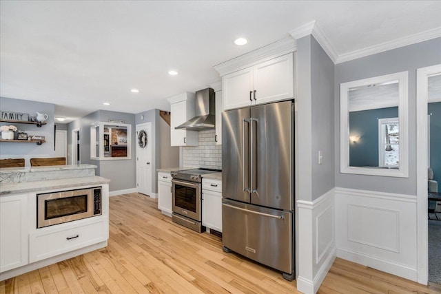 kitchen featuring a wainscoted wall, white cabinetry, light wood-style floors, appliances with stainless steel finishes, and wall chimney range hood