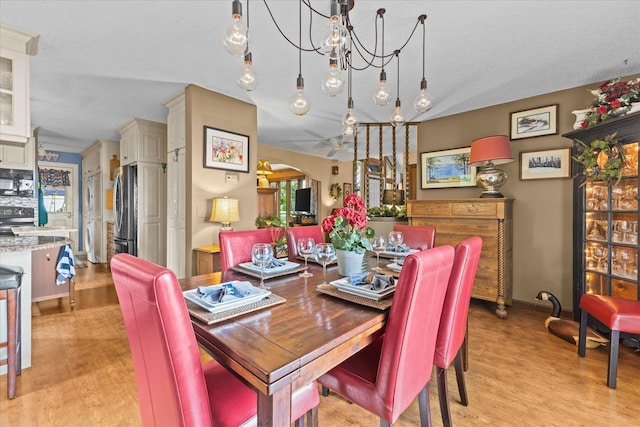 dining area featuring light wood-type flooring, an inviting chandelier, and arched walkways