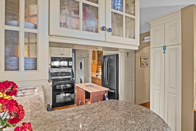 kitchen with light stone countertops, black appliances, and stacked washing maching and dryer