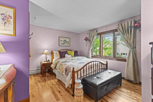 bedroom with a baseboard heating unit and light wood finished floors