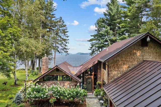 view of front of house featuring a water view, a standing seam roof, a chimney, and metal roof