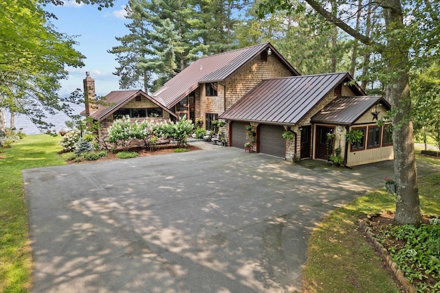 view of front of property with aphalt driveway, a chimney, an attached garage, a standing seam roof, and metal roof