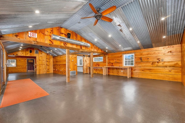 interior space featuring ceiling fan, wood walls, visible vents, vaulted ceiling, and finished concrete floors