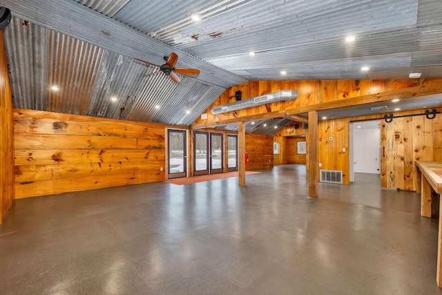 interior space with finished concrete flooring, visible vents, a ceiling fan, vaulted ceiling, and wood walls