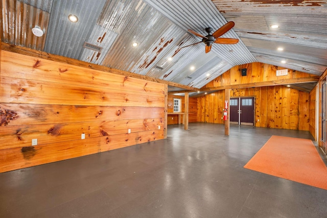 interior space with lofted ceiling, concrete flooring, wooden walls, a ceiling fan, and visible vents