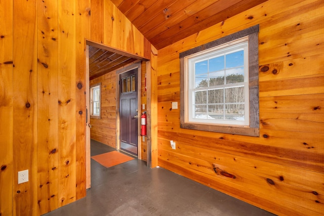 spare room featuring a healthy amount of sunlight, wooden ceiling, finished concrete floors, and wooden walls