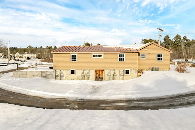 snow covered rear of property featuring an outbuilding, central air condition unit, a standing seam roof, metal roof, and a barn