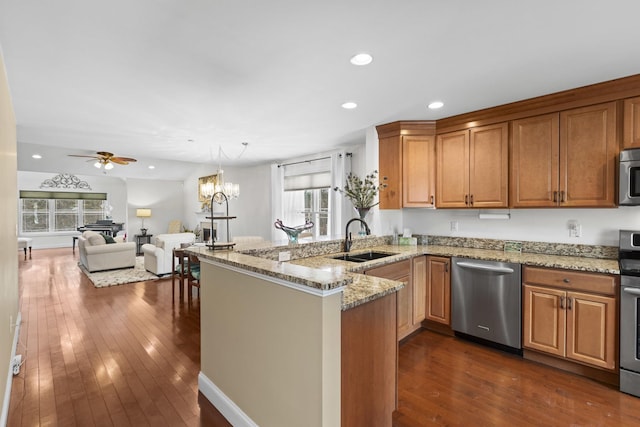 kitchen featuring appliances with stainless steel finishes, brown cabinets, dark wood-style flooring, a peninsula, and a sink