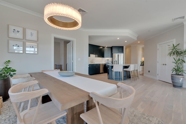 dining room with light wood-style floors, visible vents, and crown molding