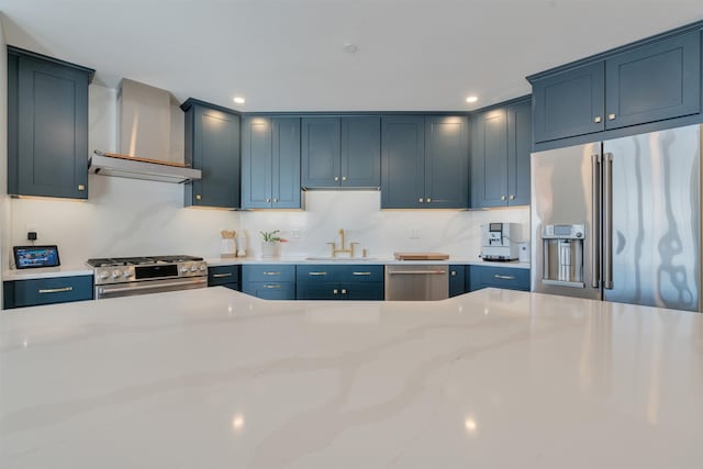 kitchen with stainless steel appliances, a sink, wall chimney exhaust hood, and light stone countertops