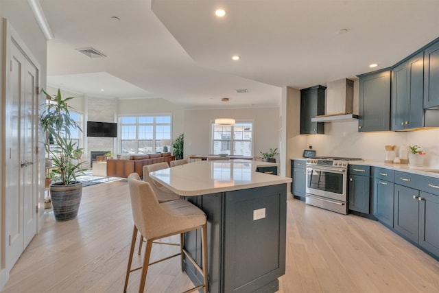 kitchen with a center island, gas stove, a large fireplace, wall chimney range hood, and light wood-type flooring