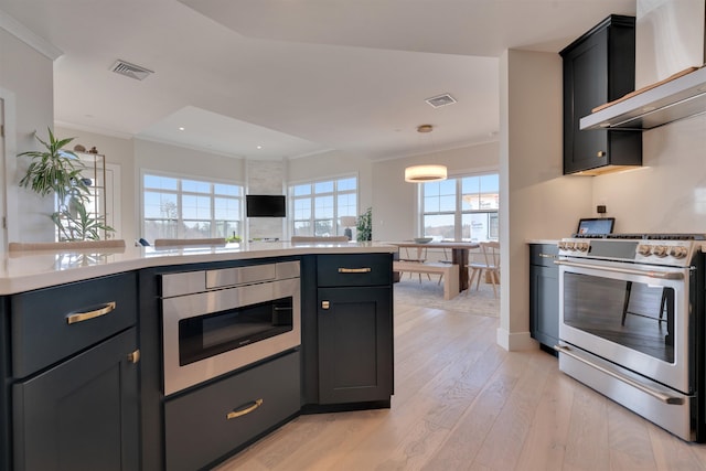 kitchen featuring visible vents, light countertops, wall chimney range hood, gas range, and light wood-type flooring