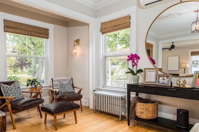 sitting room with radiator, light wood finished floors, a healthy amount of sunlight, and crown molding