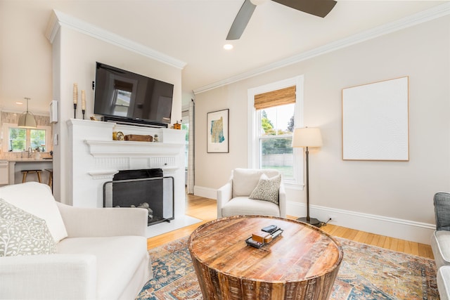 living room with baseboards, light wood-style flooring, a fireplace with flush hearth, ornamental molding, and recessed lighting