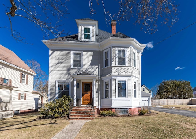 view of front of home with a garage, aphalt driveway, a chimney, and a front lawn