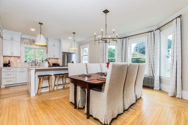 dining area featuring radiator, an inviting chandelier, ornamental molding, light wood-style floors, and baseboards