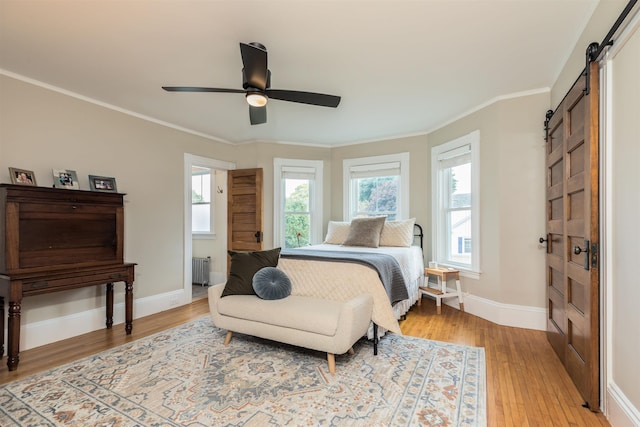 bedroom featuring ornamental molding, a barn door, light wood-style flooring, and baseboards