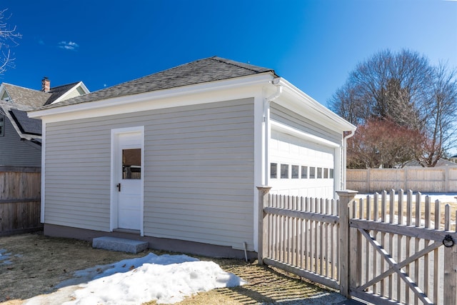 exterior space with an outbuilding, a shingled roof, fence private yard, and a garage