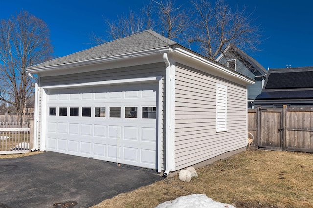 view of side of home with a garage, roof with shingles, fence, and an outdoor structure