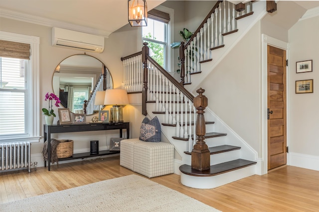 staircase with radiator, a wall unit AC, wood finished floors, an inviting chandelier, and crown molding