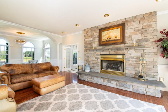 living room with crown molding, a stone fireplace, decorative columns, and wood finished floors