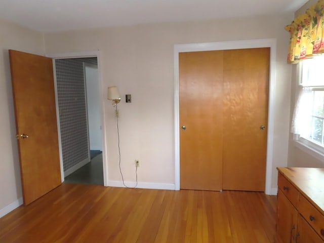 unfurnished bedroom with light wood-type flooring, a closet, and baseboards