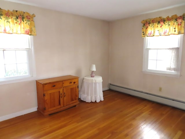 unfurnished room with a baseboard heating unit, light wood-type flooring, and baseboards