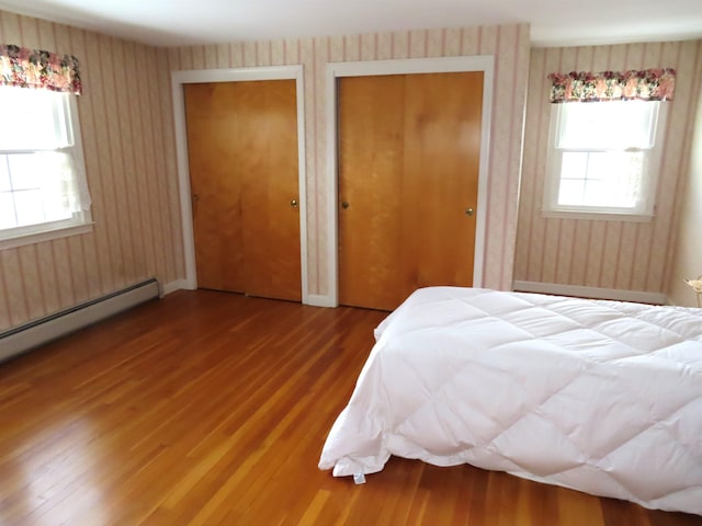 bedroom featuring two closets, a baseboard radiator, wallpapered walls, and wood finished floors