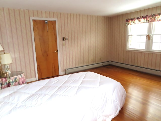 unfurnished bedroom featuring wood finished floors, baseboard heating, and wallpapered walls