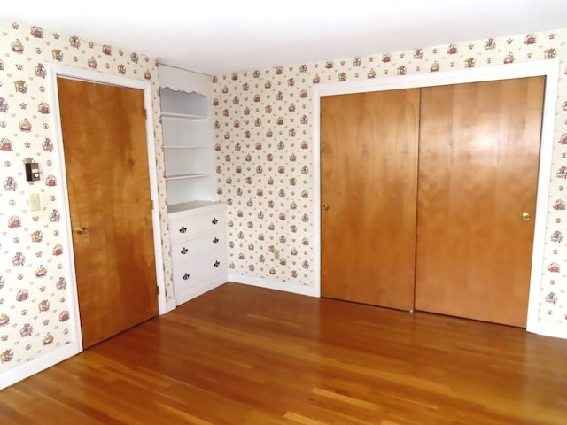 unfurnished bedroom with wallpapered walls, a closet, baseboards, and wood finished floors