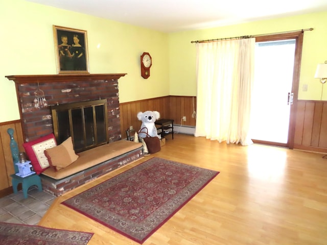 living room featuring a wainscoted wall, wooden walls, a brick fireplace, and wood finished floors