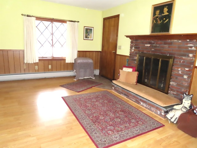 living area with a wainscoted wall, a baseboard heating unit, a fireplace, and wood finished floors