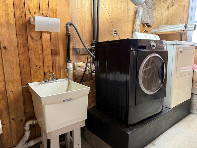 laundry area with a sink, wooden walls, and washing machine and clothes dryer