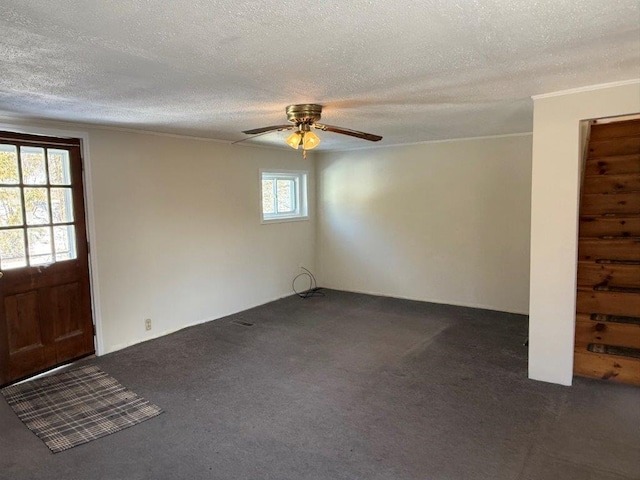 foyer entrance featuring a ceiling fan, dark colored carpet, a textured ceiling, and ornamental molding