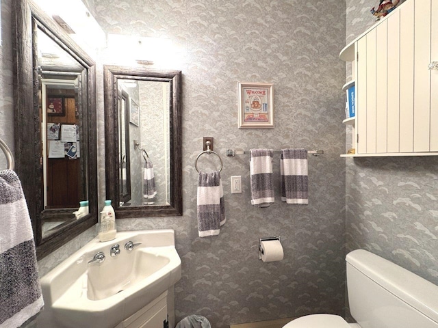 bathroom featuring toilet, wallpapered walls, and vanity