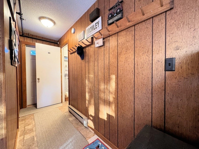 mudroom with wooden walls, baseboard heating, and a textured ceiling