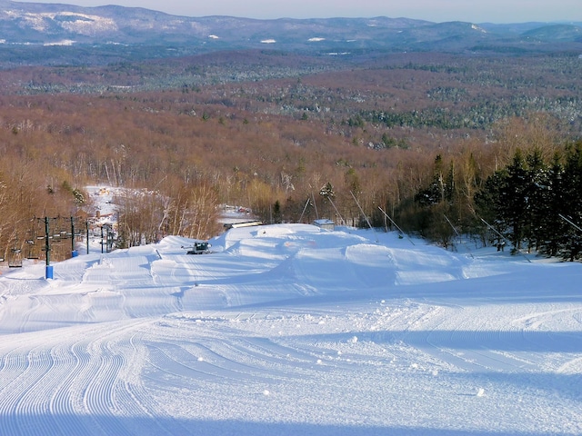 snowy aerial view featuring a forest view and a mountain view