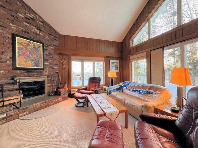 carpeted living area with plenty of natural light, high vaulted ceiling, wood walls, and a brick fireplace