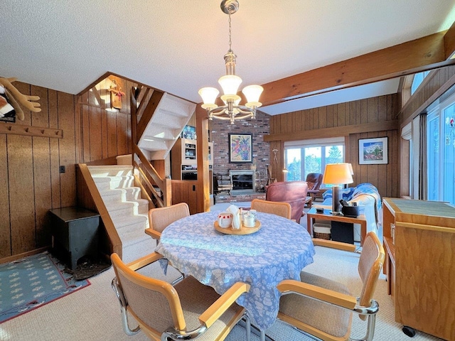 dining area featuring a brick fireplace, stairway, an inviting chandelier, carpet, and wood walls