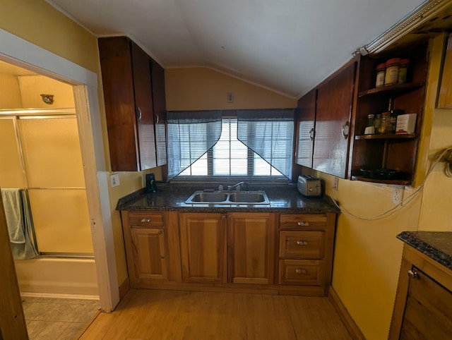 kitchen featuring light wood-style flooring, a sink, vaulted ceiling, brown cabinetry, and dark stone countertops