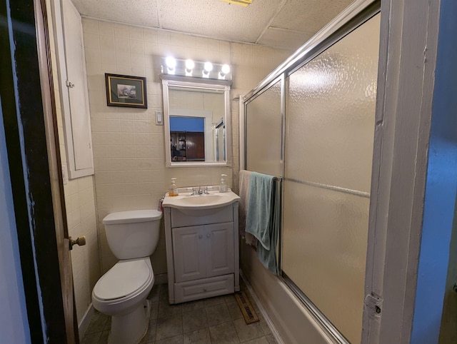 full bath with shower / bath combination with glass door, tile walls, toilet, vanity, and tile patterned flooring