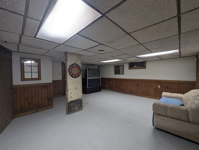 finished below grade area with a wainscoted wall, a drop ceiling, and wooden walls