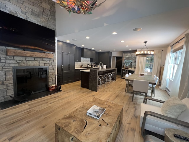 living room with light wood finished floors, an inviting chandelier, recessed lighting, a fireplace, and a baseboard heating unit