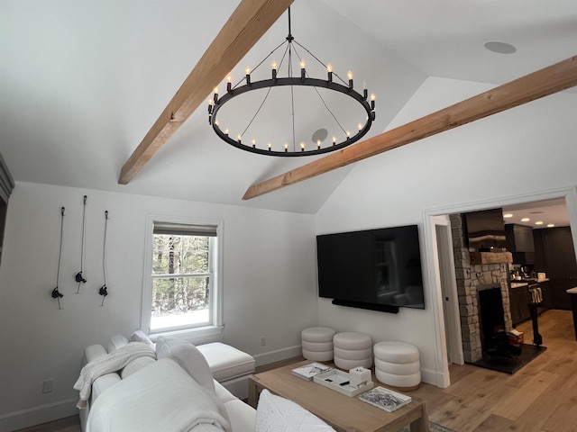 living area with wood finished floors, baseboards, lofted ceiling with beams, a stone fireplace, and a notable chandelier