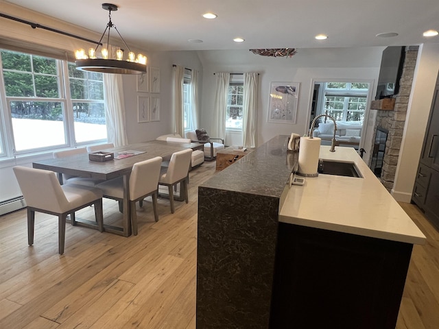 kitchen featuring pendant lighting, light wood-style floors, open floor plan, a sink, and a stone fireplace