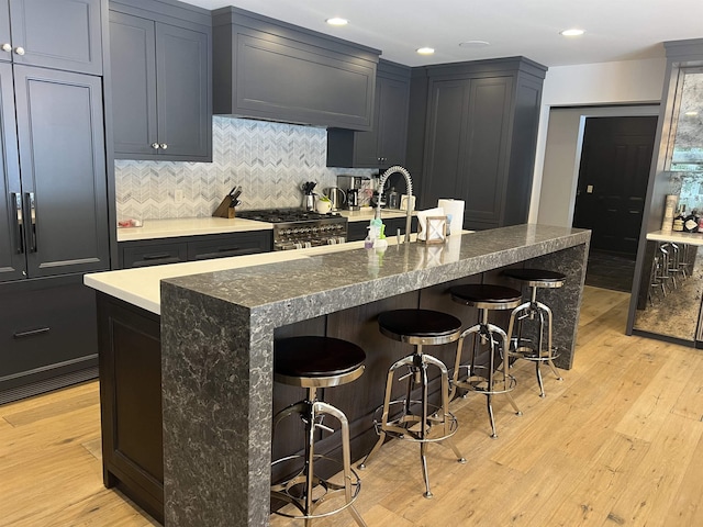 kitchen featuring light wood-type flooring, a kitchen breakfast bar, tasteful backsplash, and high end stainless steel range