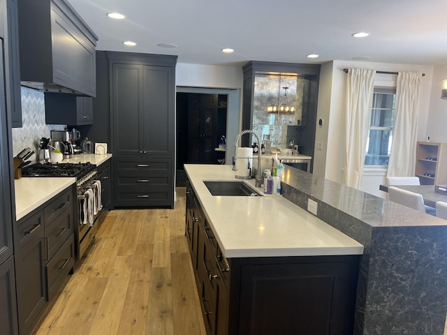 kitchen with a center island with sink, a sink, recessed lighting, stainless steel stove, and light wood finished floors